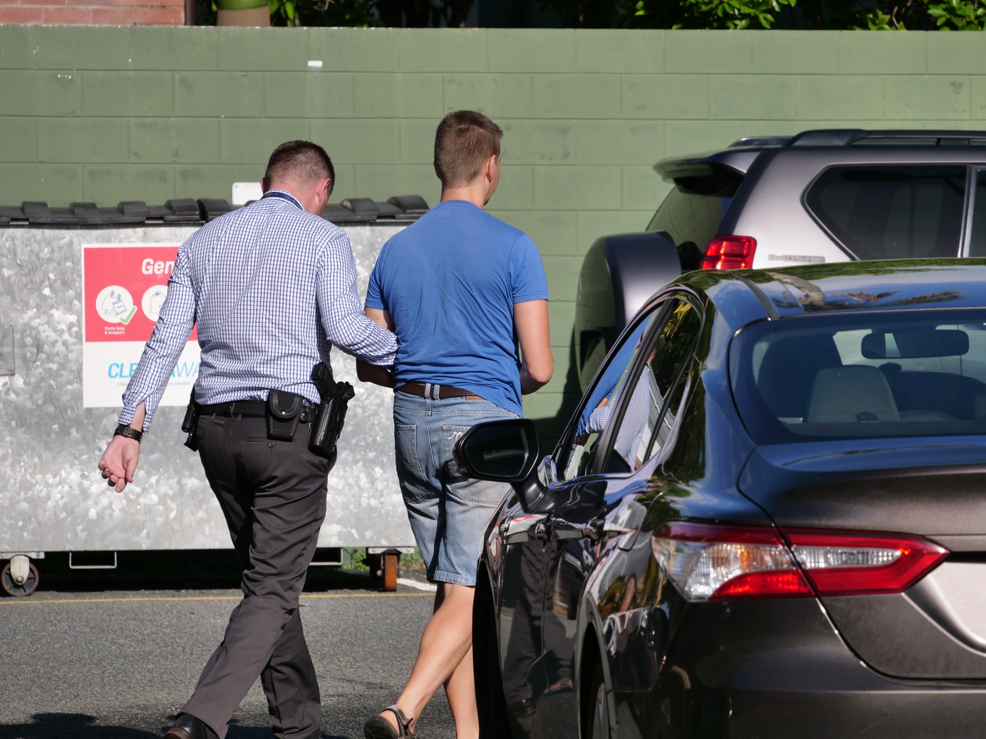 A man in a blue shirt being escorted by a detective in plain clothes. 
