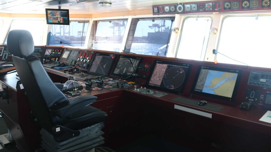 Inside the bridge of RV Sonne. The captain's chair is empty but the control panel is lit up and the harbour is visible.