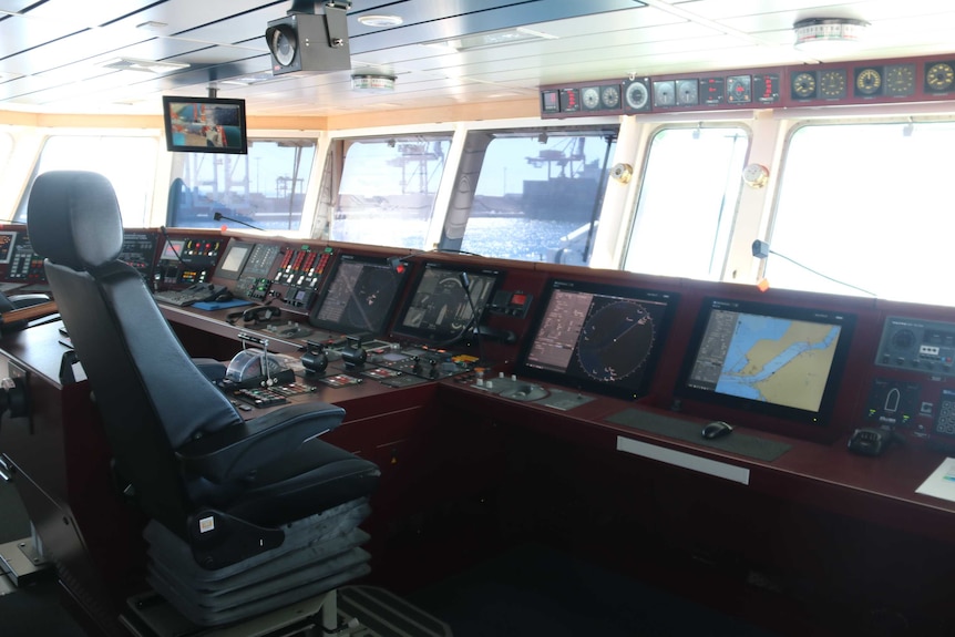 Inside the bridge of RV Sonne. The captain's chair is empty but the control panel is lit up and the harbour is visible.