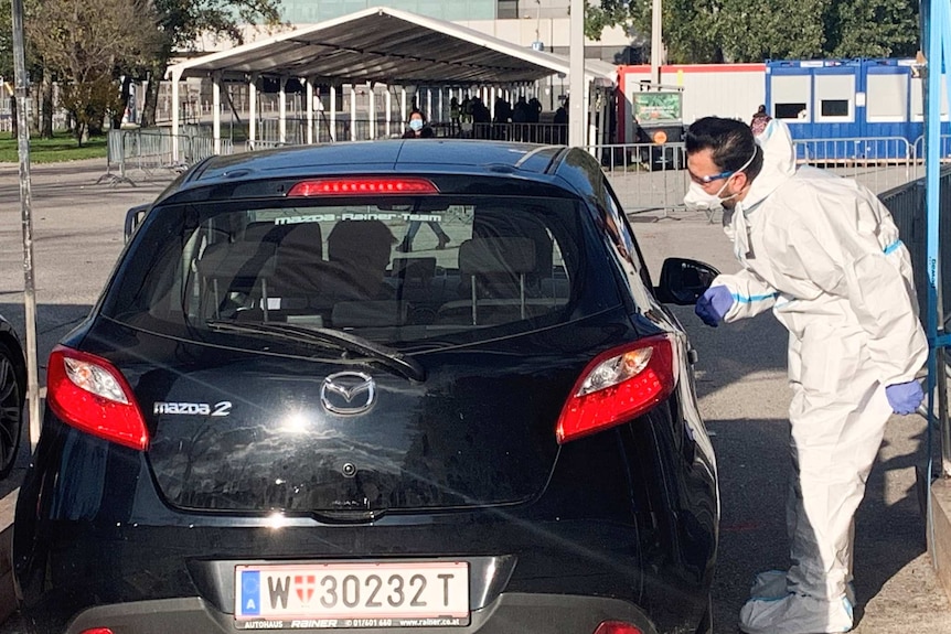 A testing official leans into a car at a drive-through COVID-19 tests site in Vienna.