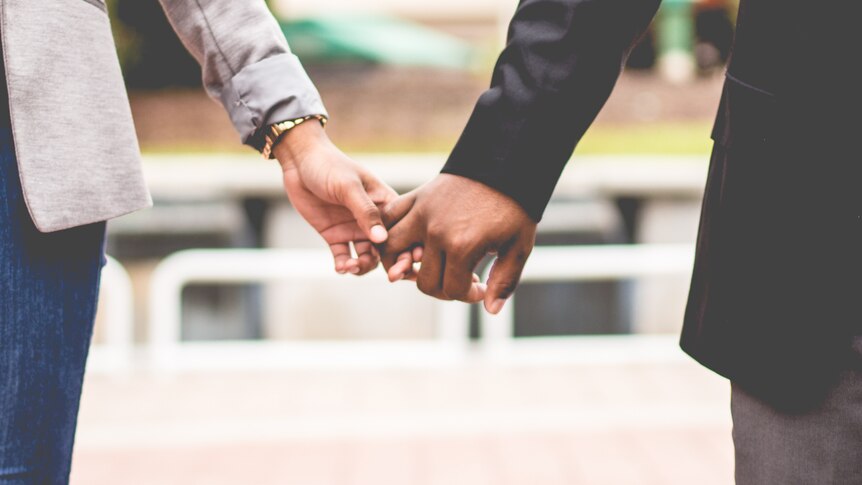 Two people holding hands representing the stress of hiding a workplace sexual relationship.