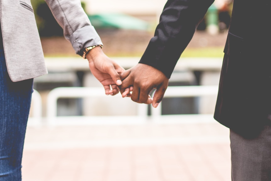 Two people holding hands representing the stress of hiding a workplace sexual relationship.