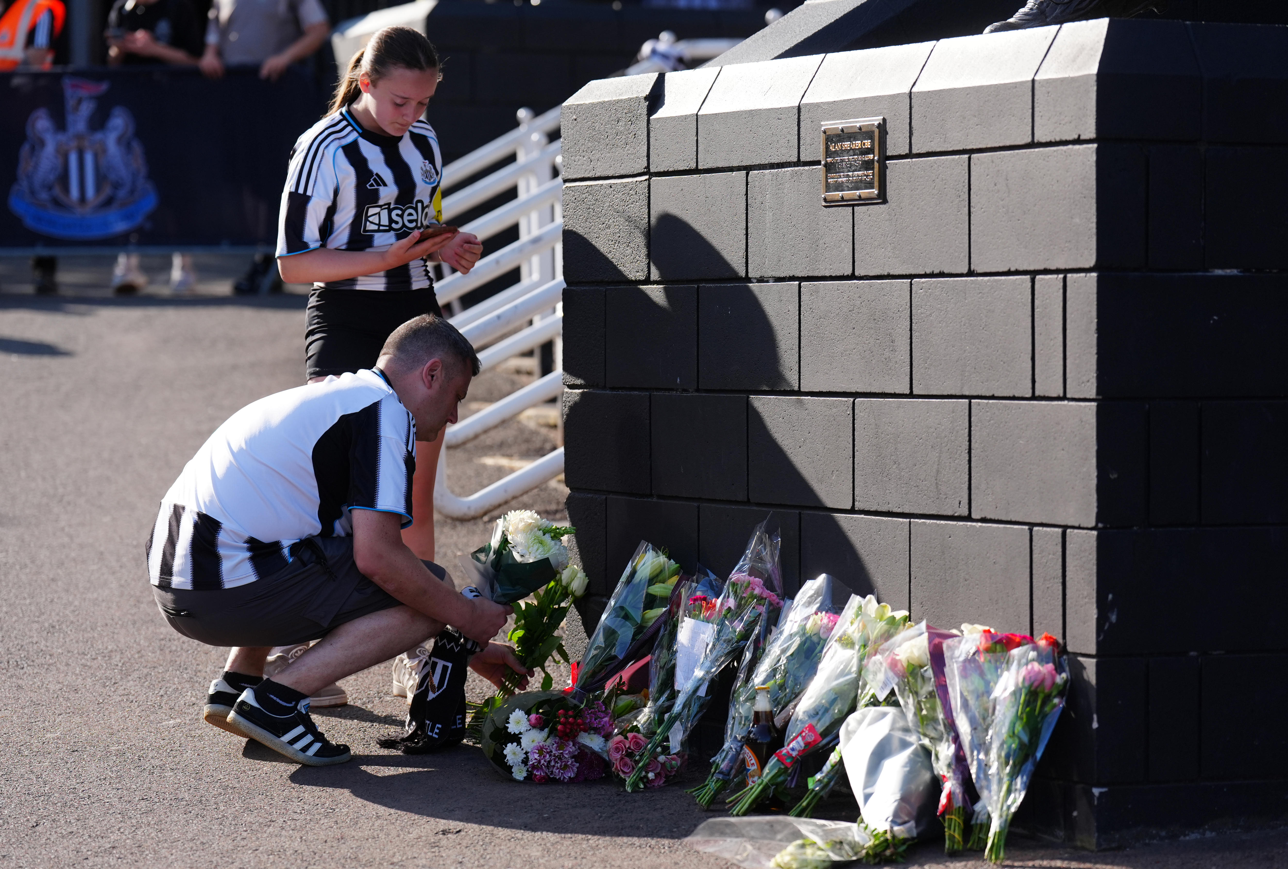 A man and a woman in black-and-white striped football shirts lay flowers atthe base of a statue.