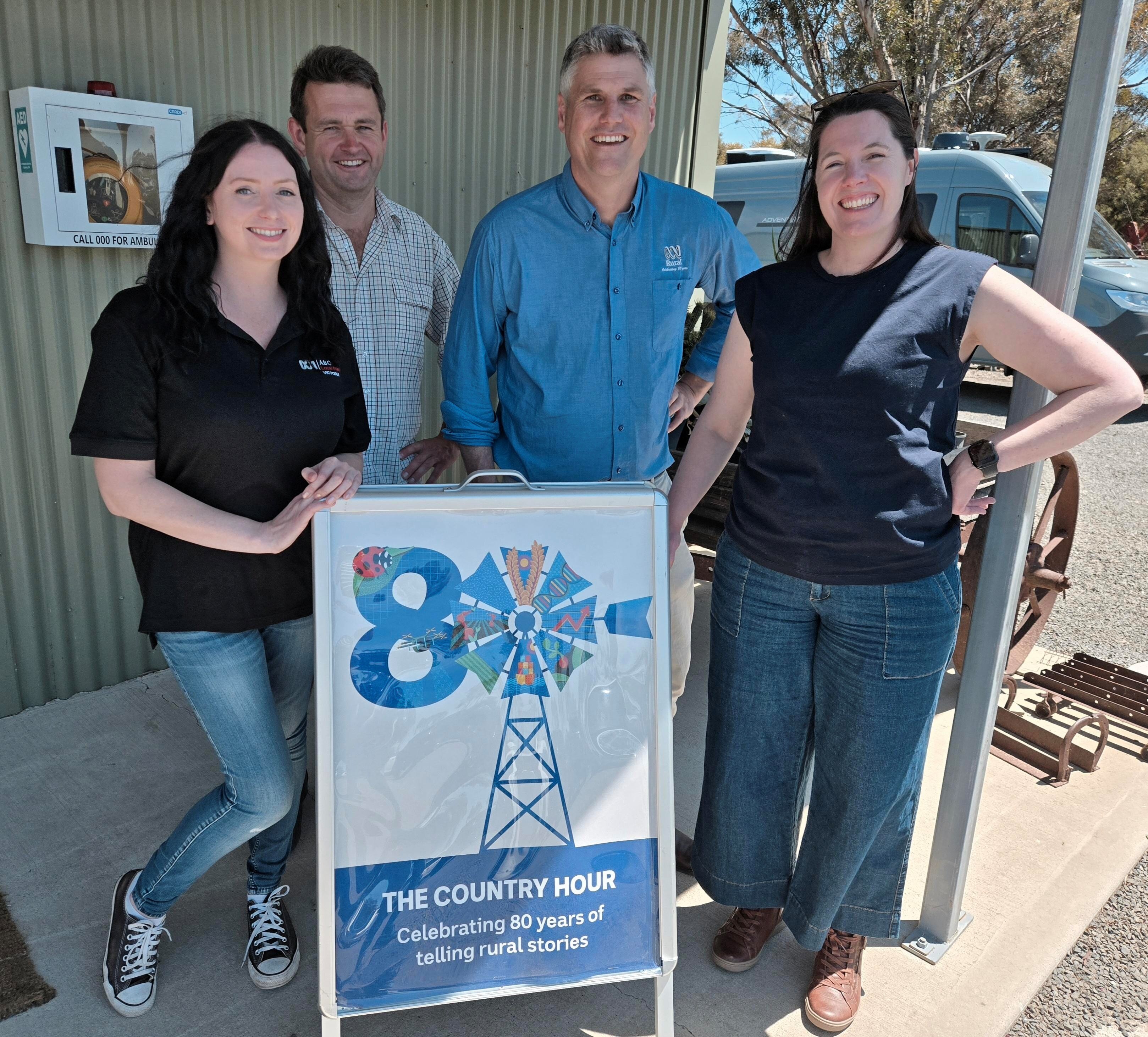 a woman, two men and a a woman with a 80th year country hour sign 