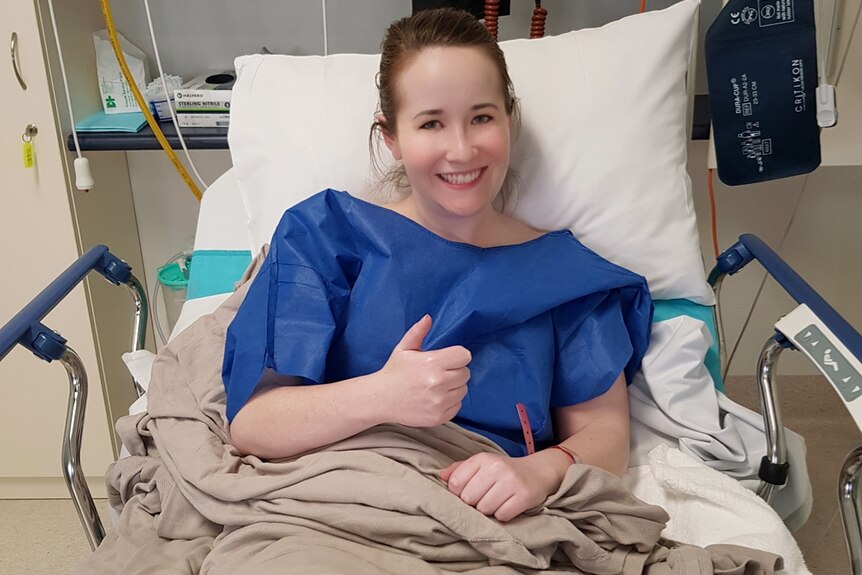 Jacinta smiling and giving the thumbs up from a hospital bed.