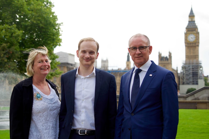 A woman  and two men standing in front of a lush green lawn with Big Ben visible in the background.