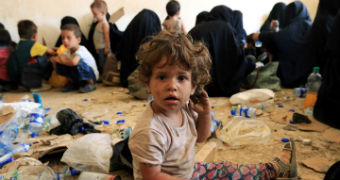 A toddler covered in dirt sits amongst piles of rubbish.