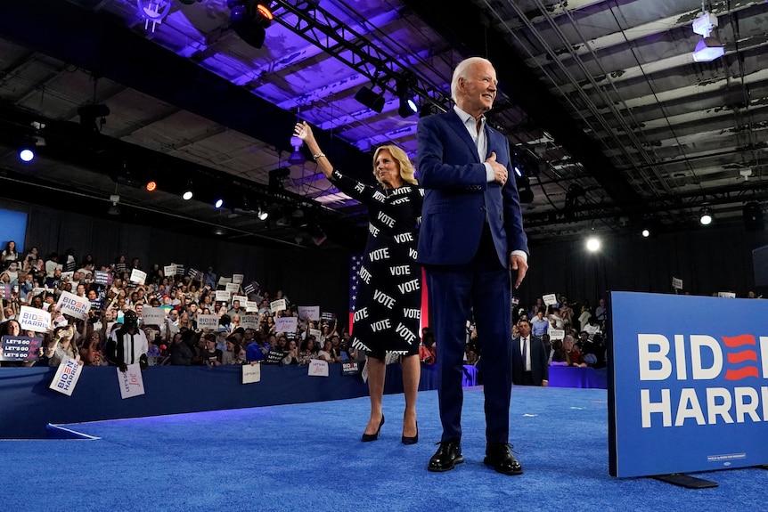 Joe Biden and Jill Biden wave on a stage to fans with signs at a campaign event