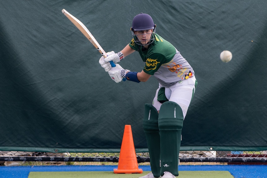 A male cricketer hold his bat ready to hit a white ball