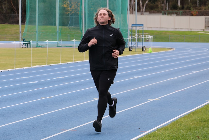 Jam is wearing black sports clothing and is running on a blue racing track.