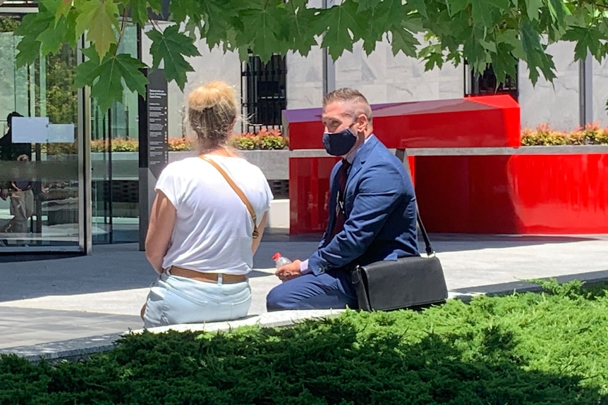 A man in a blue suit sits next to a woman with her back to the camera.