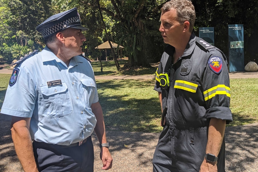 Police officer and fire officer stand in a park talking.