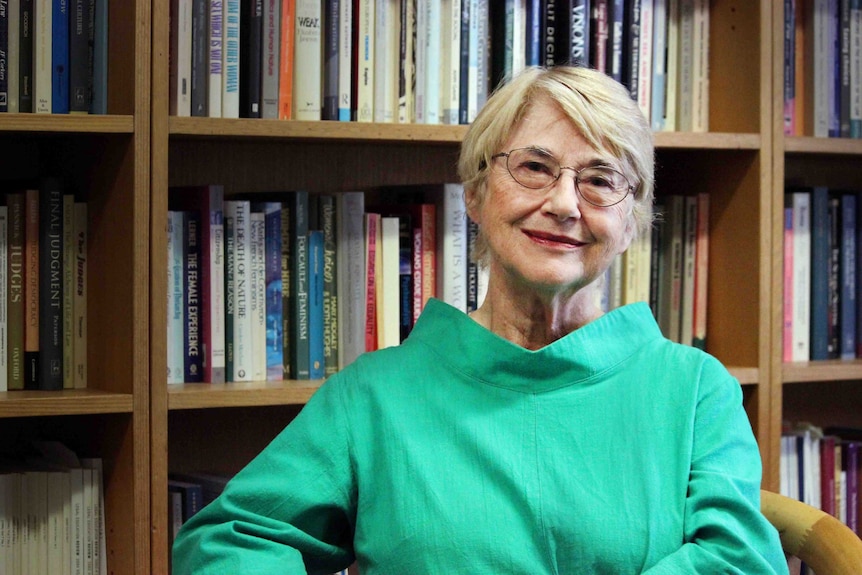 Woman in fabulous green top sits in front of book shelf