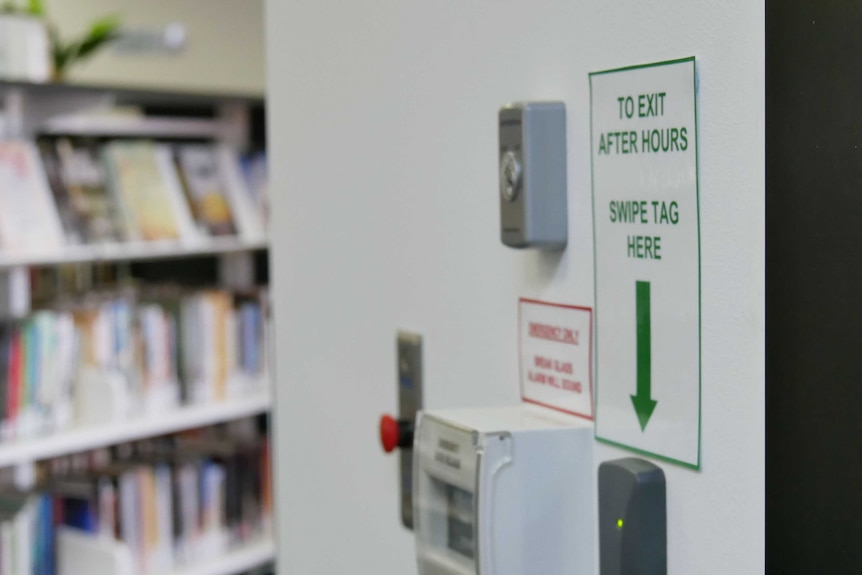 A close-up of swipe access next to a door, there are library books out of focus in the background.