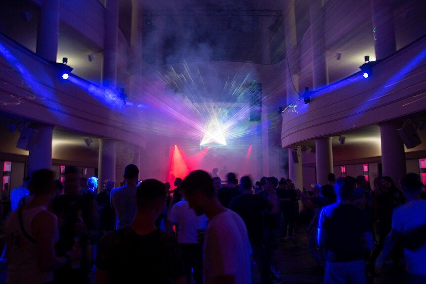A dark crowded dance floor with laser lights streaming through the space. 