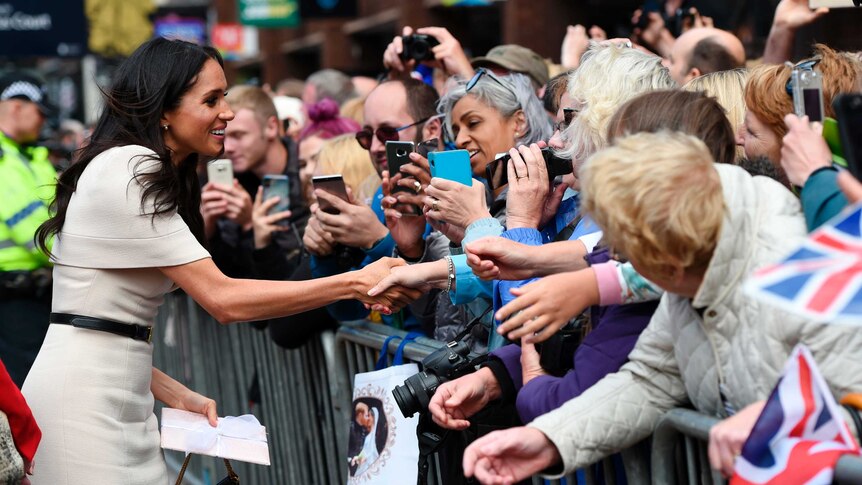 Meghan, Duchess of Sussex shakes hands with a fan as she walks along a street.