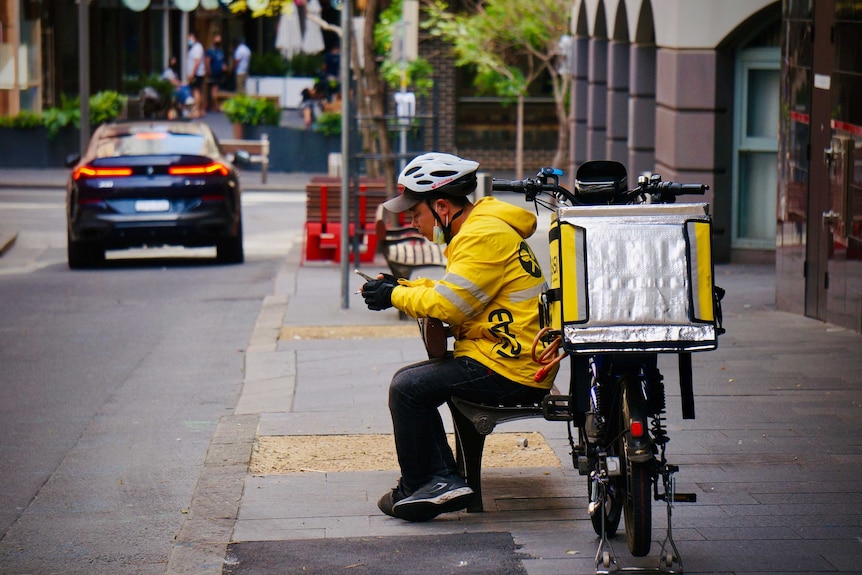 A delivery rider rests on a street bench in Sydney.