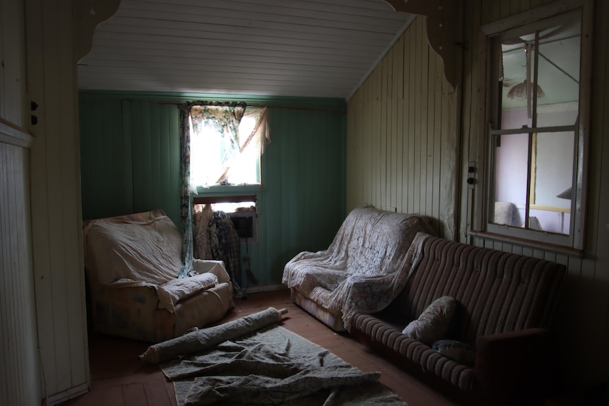An old room, with dilapidated furniture and fabric strewn across the room.