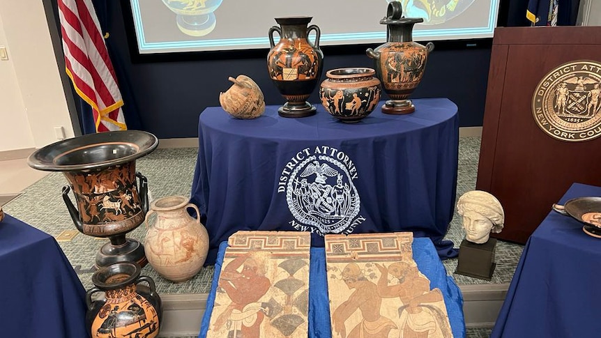An array of antiquities including Etruscan vases and ancient Roman coins and mosaics laid out at a press conference. 