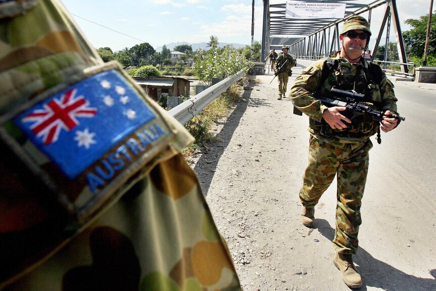 Armed Australian peacekeepers march across a bridge