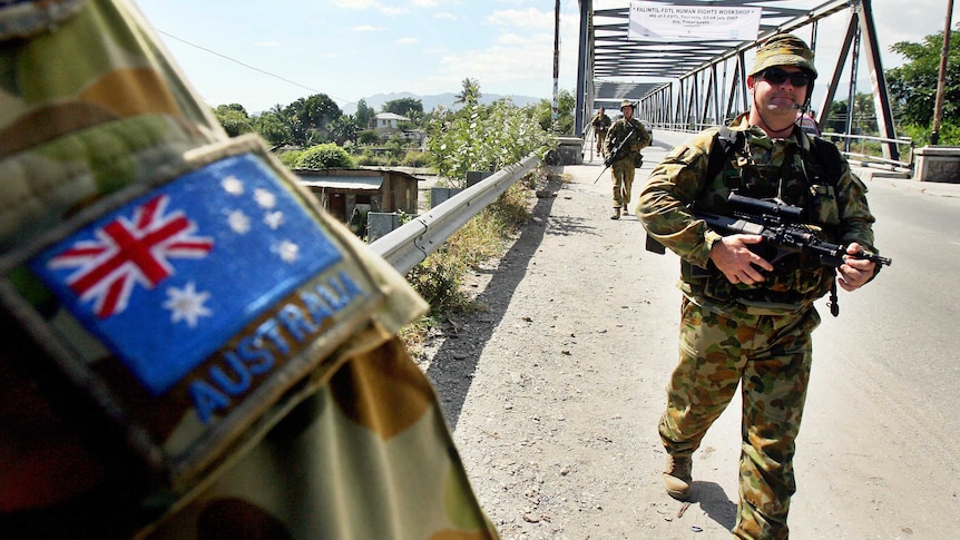Armed Australian peacekeepers march across a bridge