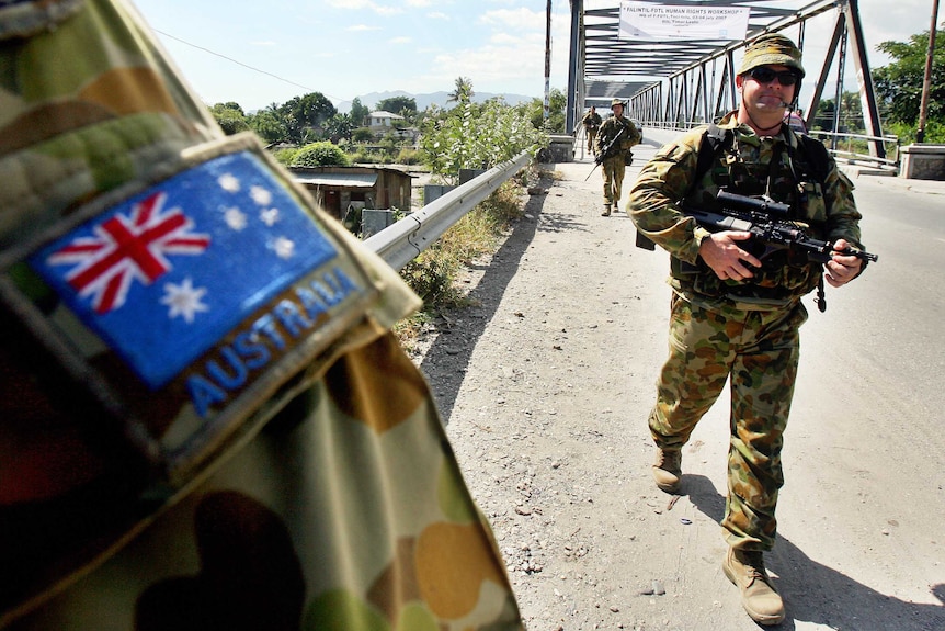 Armed Australian peacekeepers march across a bridge