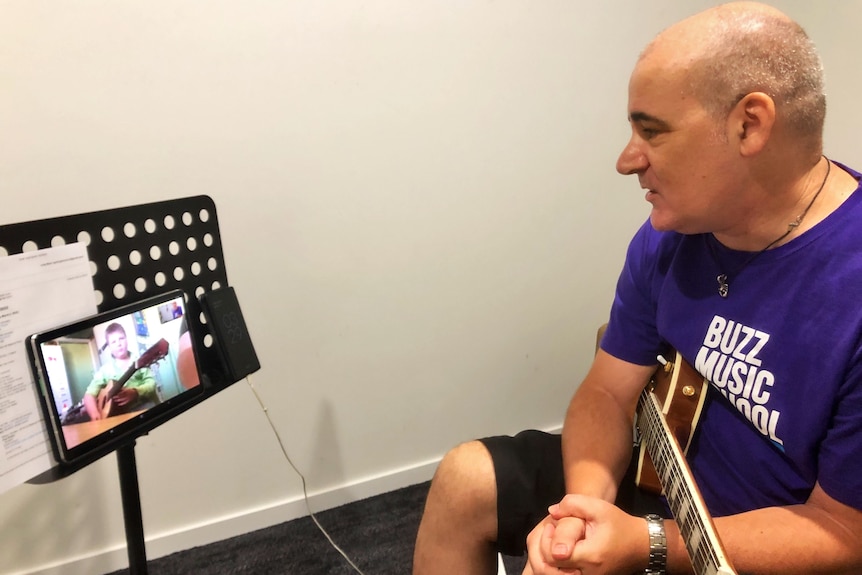 A man with a guitar looks at a computer screen.