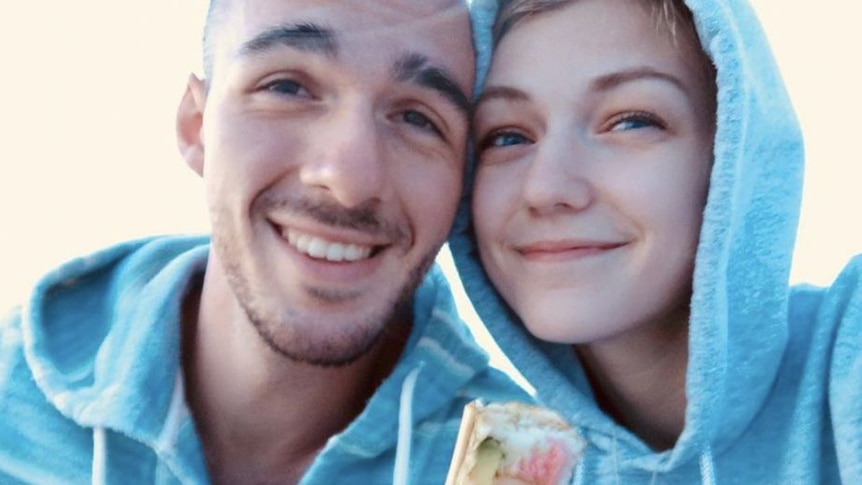 A young bald man and young woman with blonde hair wearing grey hoodies smiling
