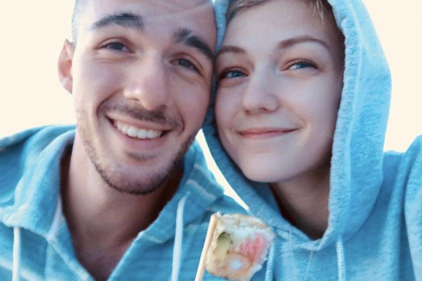 A young bald man and young woman with blonde hair wearing grey hoodies smiling