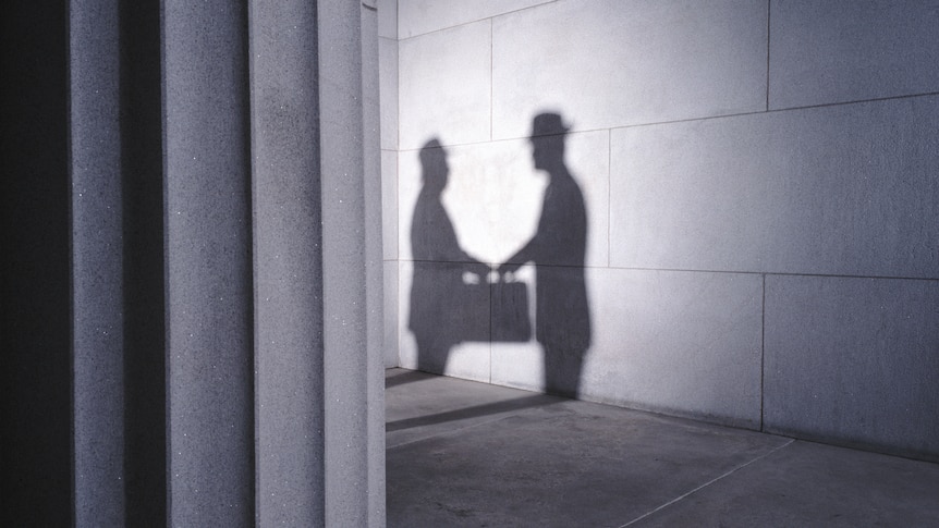 The shadows of two men with briefcases shaking hands.