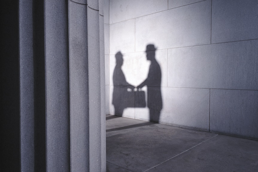 The shadows of two men with briefcases shaking hands.