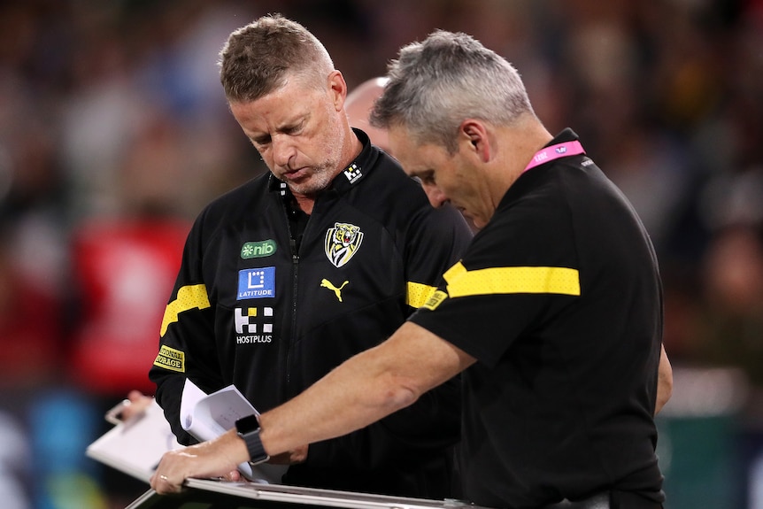 Damien Hardwick looks at a board as he speaks to a Richmond assistant coach during a match.