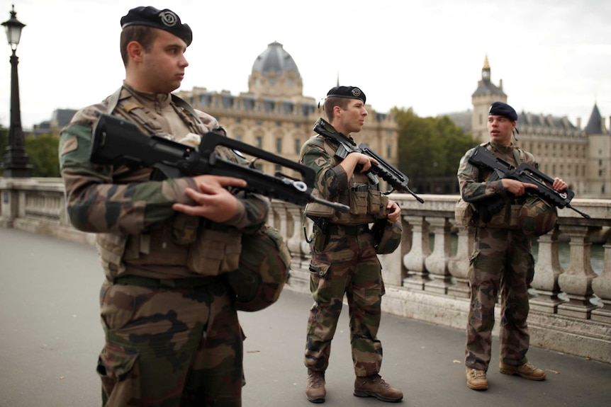 Three heavily armed soldiers guard a bridge