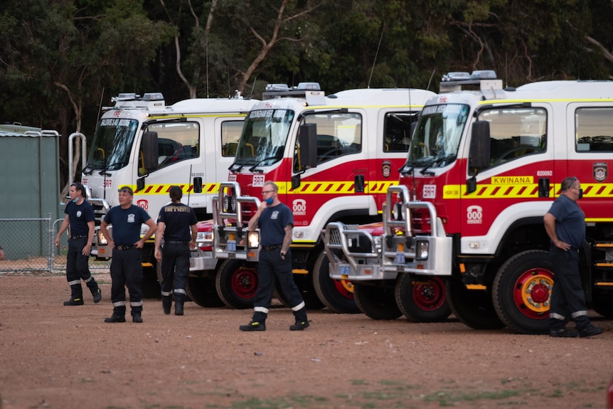 Firefighters standing next to fire trucks