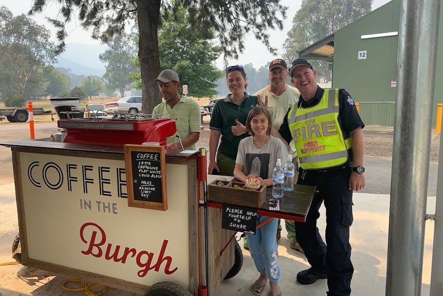 man making coffee stands next to child and emergency service personnel 