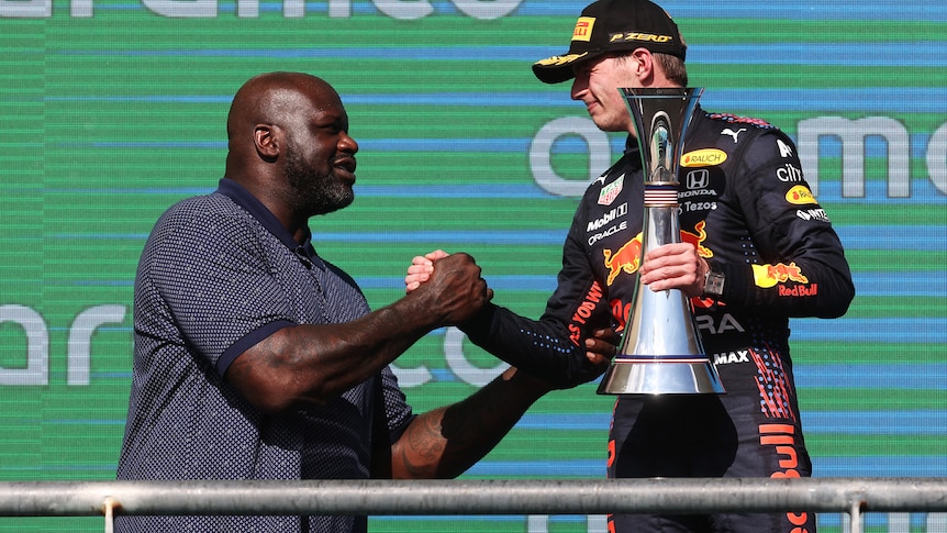 Max Verstappen shakes hands with Shaquille O'Neal while holding a big trophy