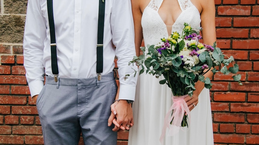 A newly married couple hold hands at their wedding.