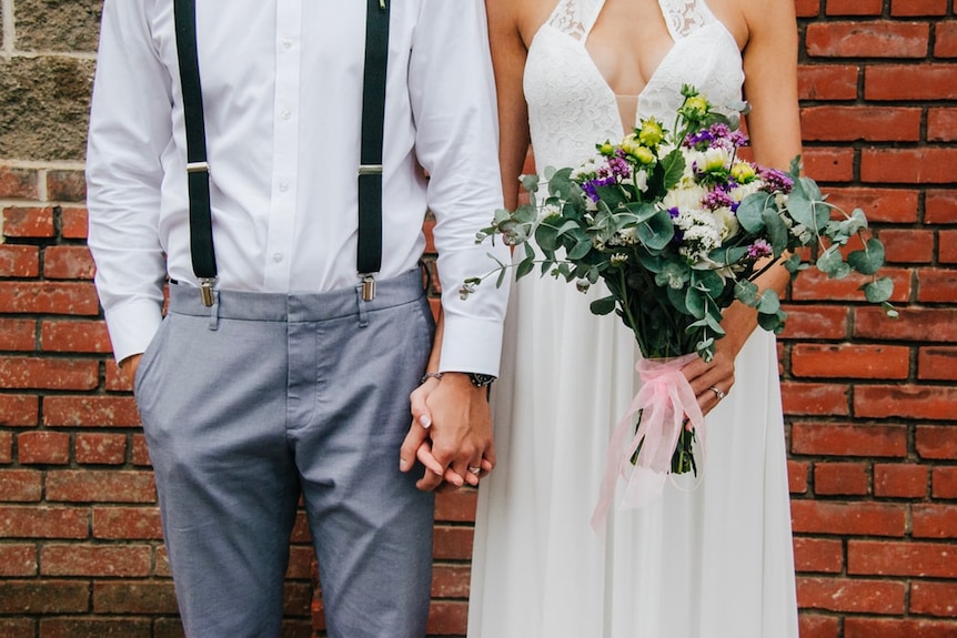 A newly married couple hold hands at their wedding.