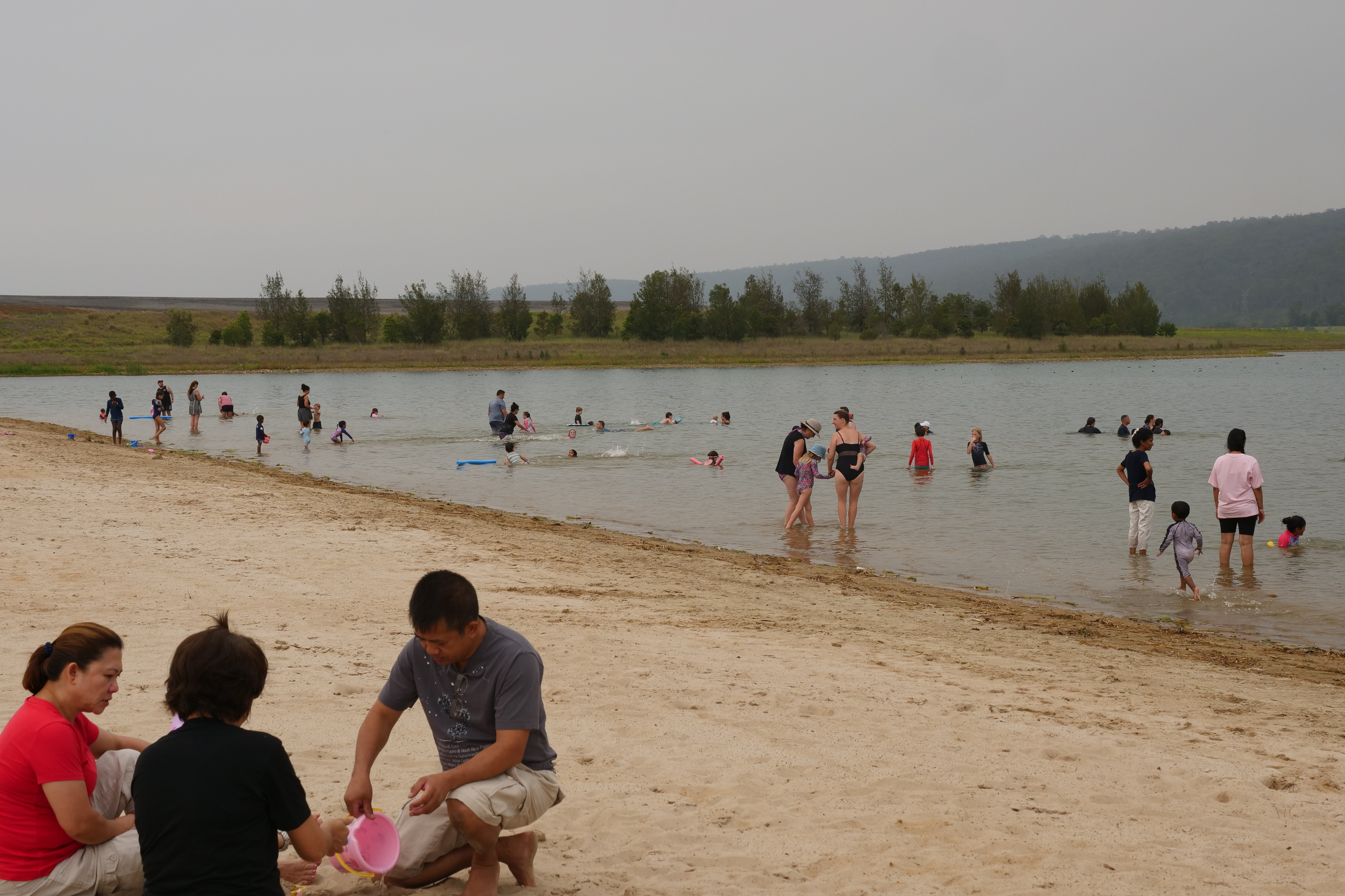 Una familia construye un castillo de arena con flotadores en el agua al fondo. 
