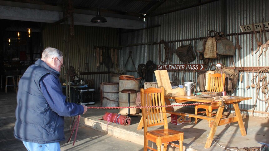 Man standing stretching a leather rein in a workshop.