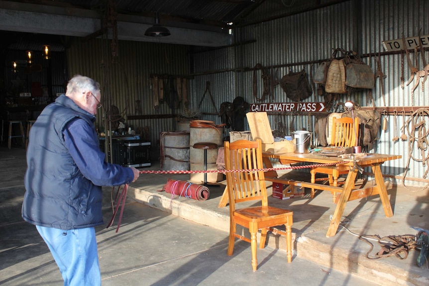 Man standing stretching a leather rein in a workshop.