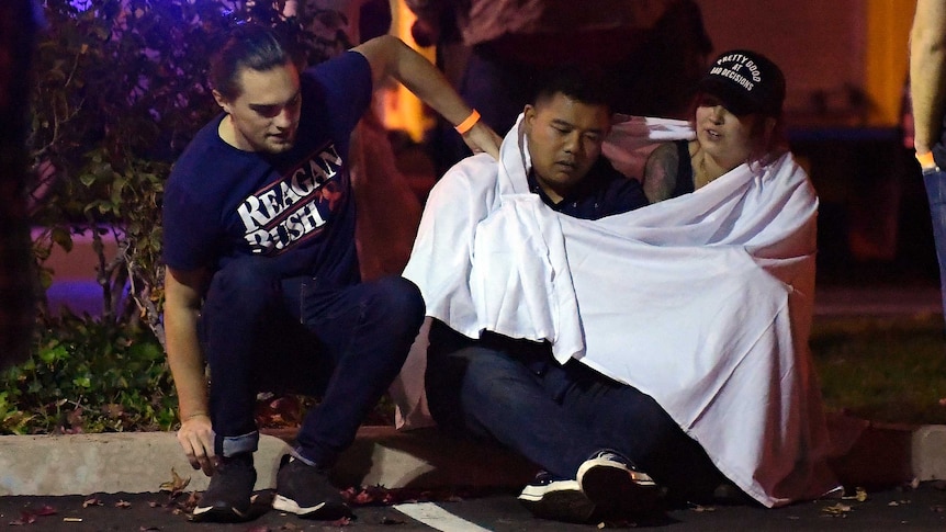 People sit on the ground wrapped in blankets after a mass shooting at a bar in California.