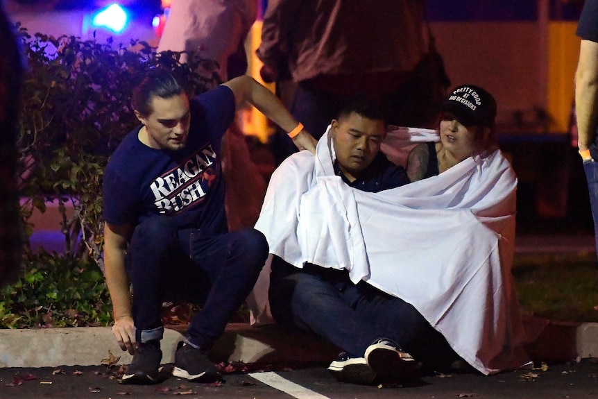 People sit on the ground wrapped in blankets after a mass shooting at a bar in California.