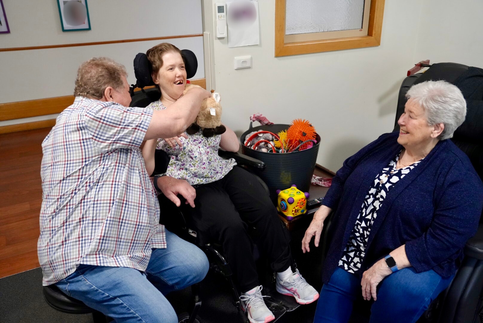 Karen está sentada en una silla de ruedas con sus padres. Los tres sonríen.