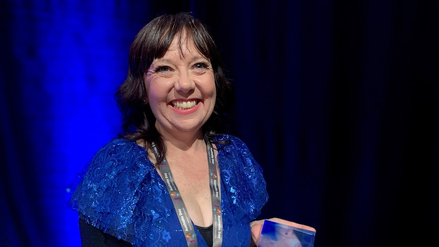 A woman in a blue dress smiles while holding an award on stage