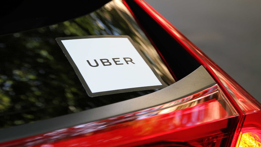 An Uber sign on the back window of a red car.