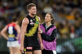 A Richmond player looks emotional as he stands on the ground while a medic puts her hand on his arm.