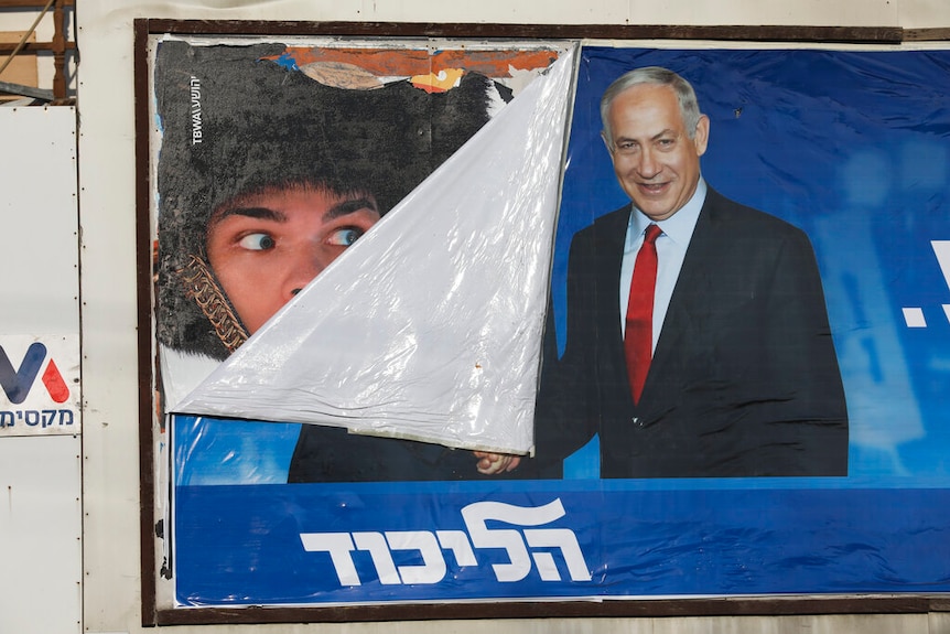 A campaign poster of Benjamin Netanyahu is partially coming down, with Netanyahu shown shaking the hand of someone obscured.