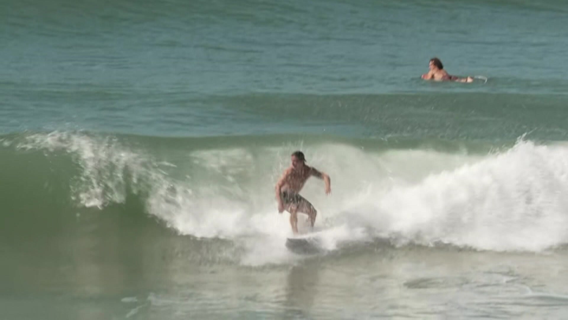 A shirtless man in boardshorts cuts across a wave on a surfboard.