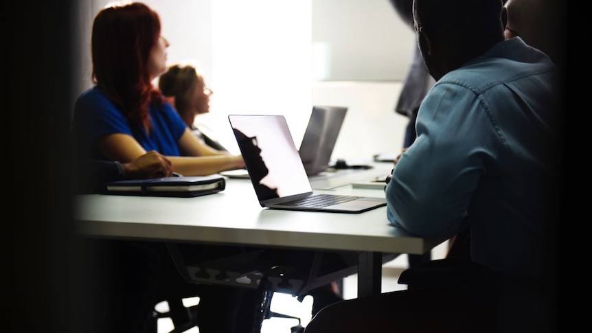 Two women and two men in a meeting. Some have laptops on the table in front of them.